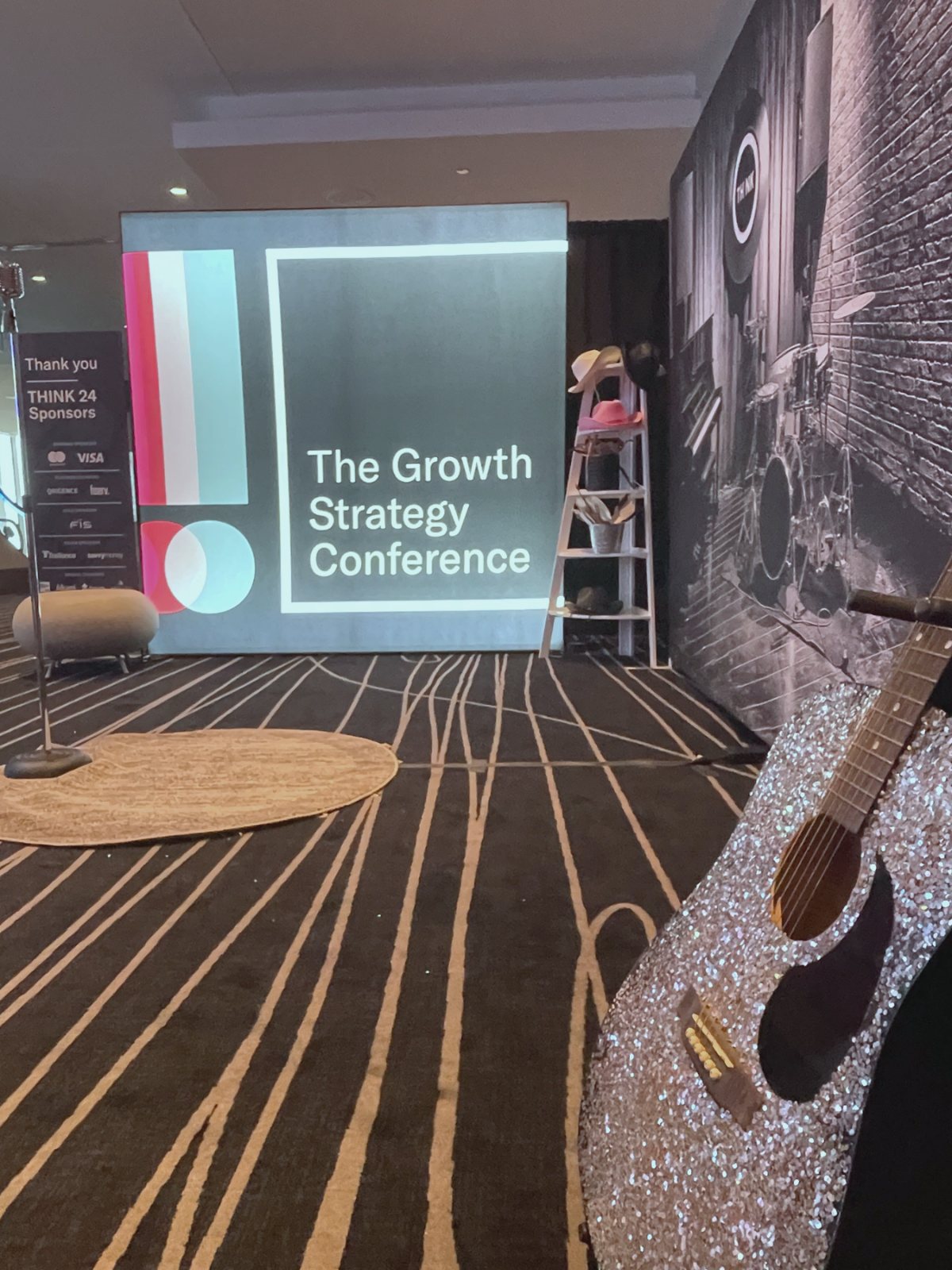 A THINK 24 pop-up studio set, with the illuminated Growth Strategy Conference panel, a rhinestone guitar and the honky-tonk wall behind it.