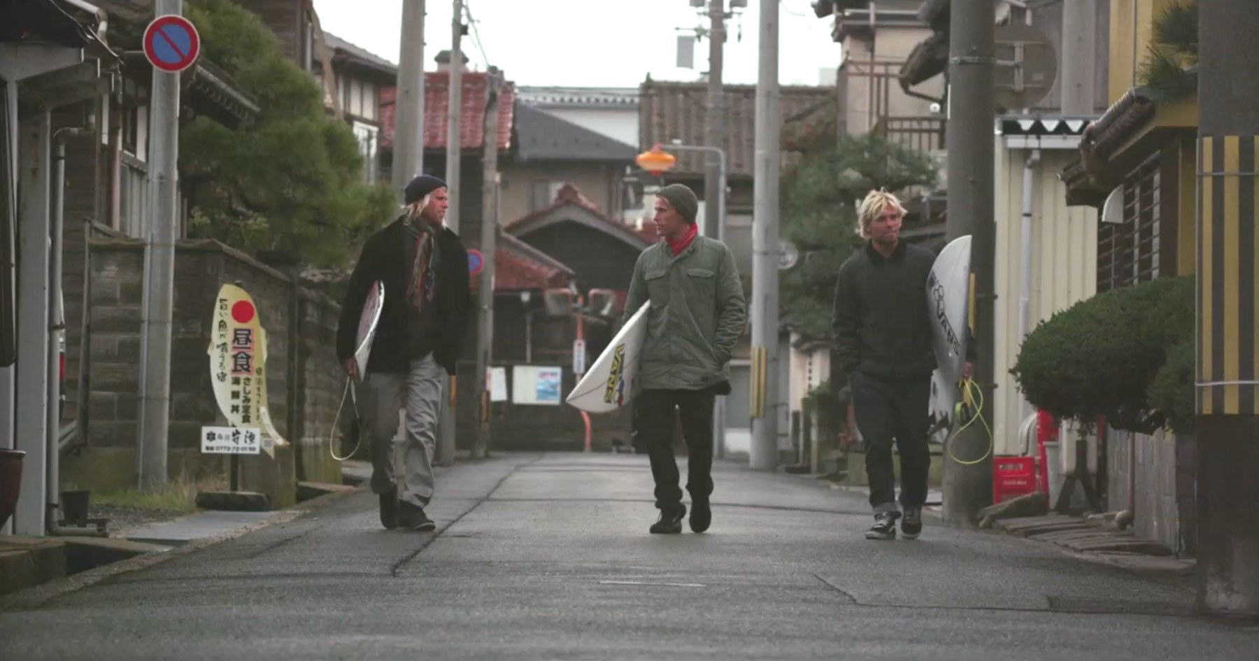 Three Vans surfers carrying boards down a residential street in Japan, from the Down Days series